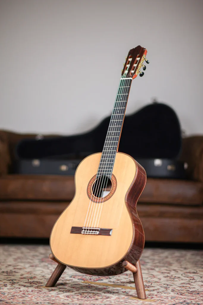 Classical acoustic guitar with nylon strings and spruce top on a wooden stand with a hard case background.