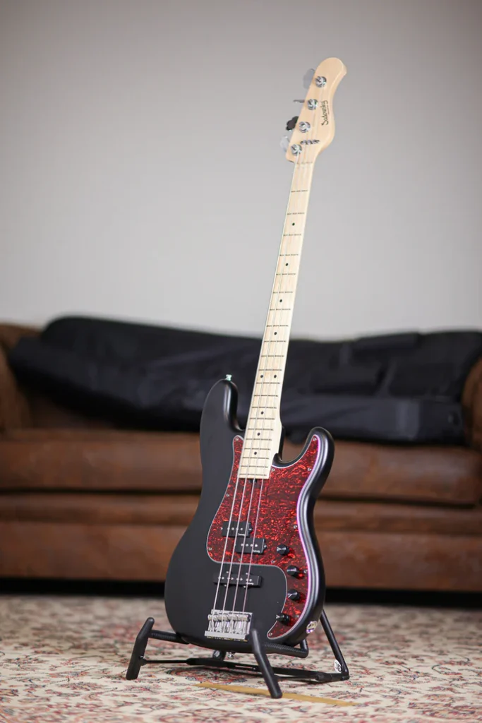 Sadowsky MetroLine 4-string electric bass guitar in matte black with red tortoise pickguard on a stand.