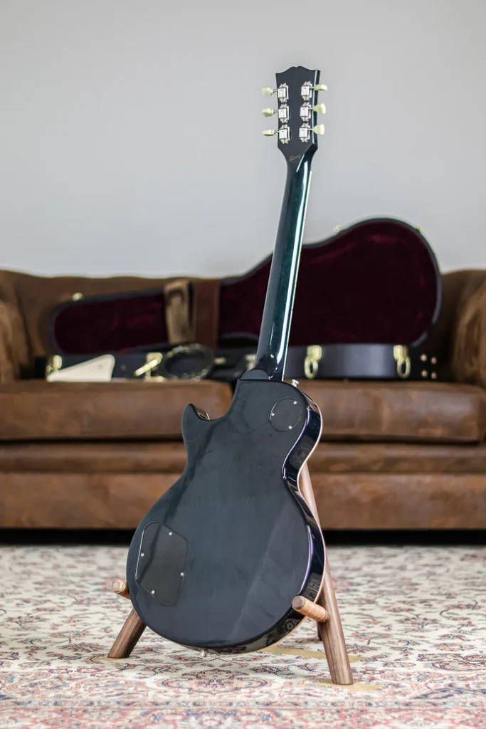 Back view of a Gibson Les Paul electric guitar in dark finish on a wooden stand with hardshell case background.