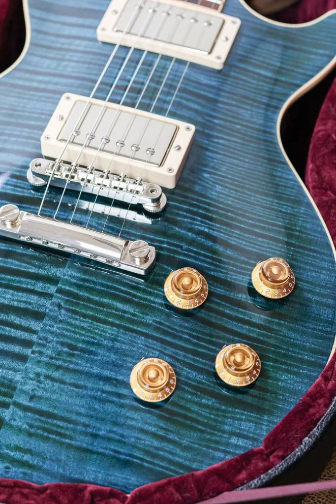 Close-up of a Gibson Les Paul electric guitar in translucent blue finish showing flamed maple top, humbucker pickups, and gold knobs.