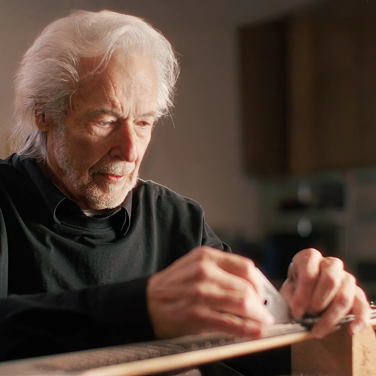 Senior guitar luthier carefully leveling frets on an electric guitar neck fretboard inside a workshop.